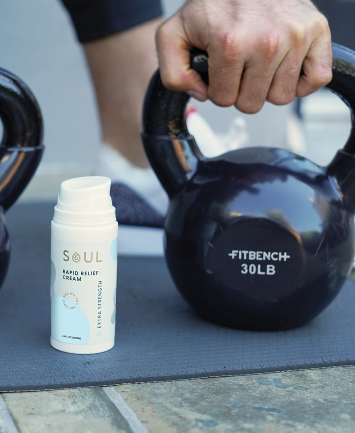 Angled view of Soul Rapid Relief Cream bottle showing label and pump with a 30 lb kettlebell on a workout mat
