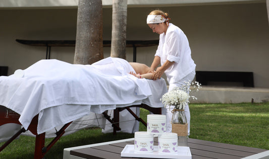 Therapist giving an outdoor massage to a client beside a table with stacked Soul soothing relief cream jars and a vase of white flowers