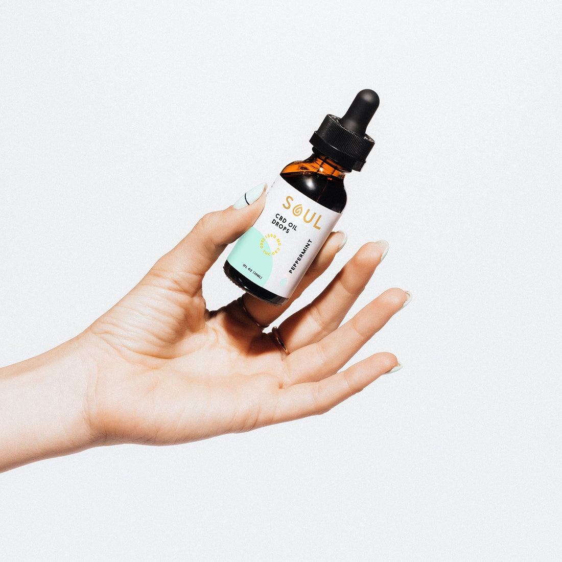Close-up of hand holding Soul peppermint CBD oil dropper bottle showcasing the label and amber glass with white background