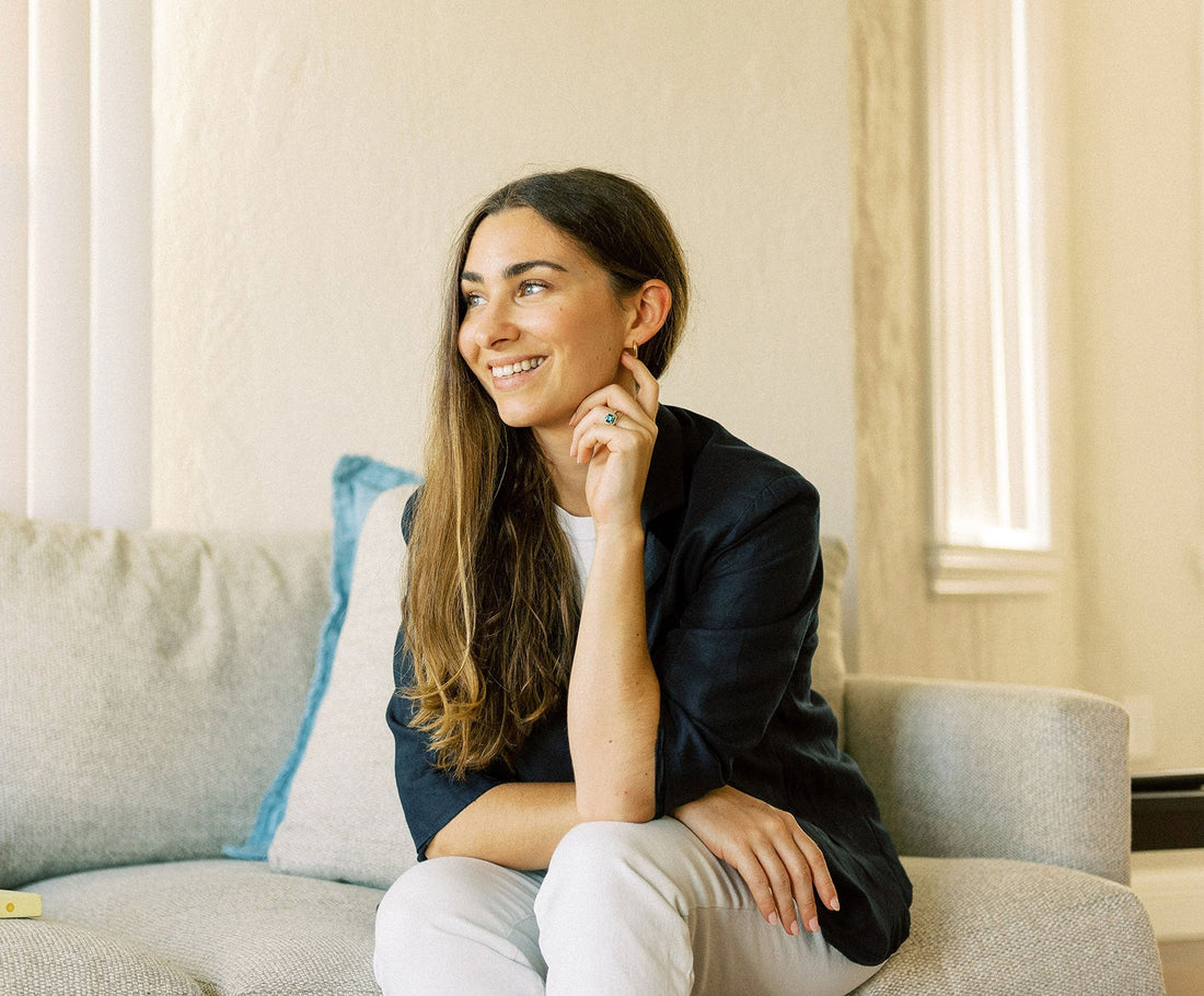 Young woman smiling and looking to the left while seated on a couch in a bright, neutral-toned living room