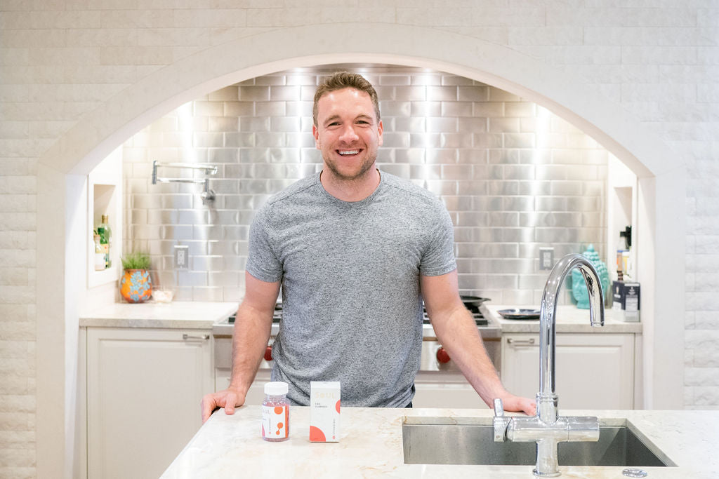 Founder smiling and leaning on a kitchen island with two supplement bottles on the counter
