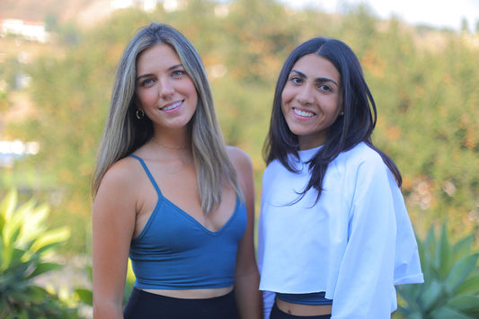 Two women smiling at the camera outdoors with a blurred green background