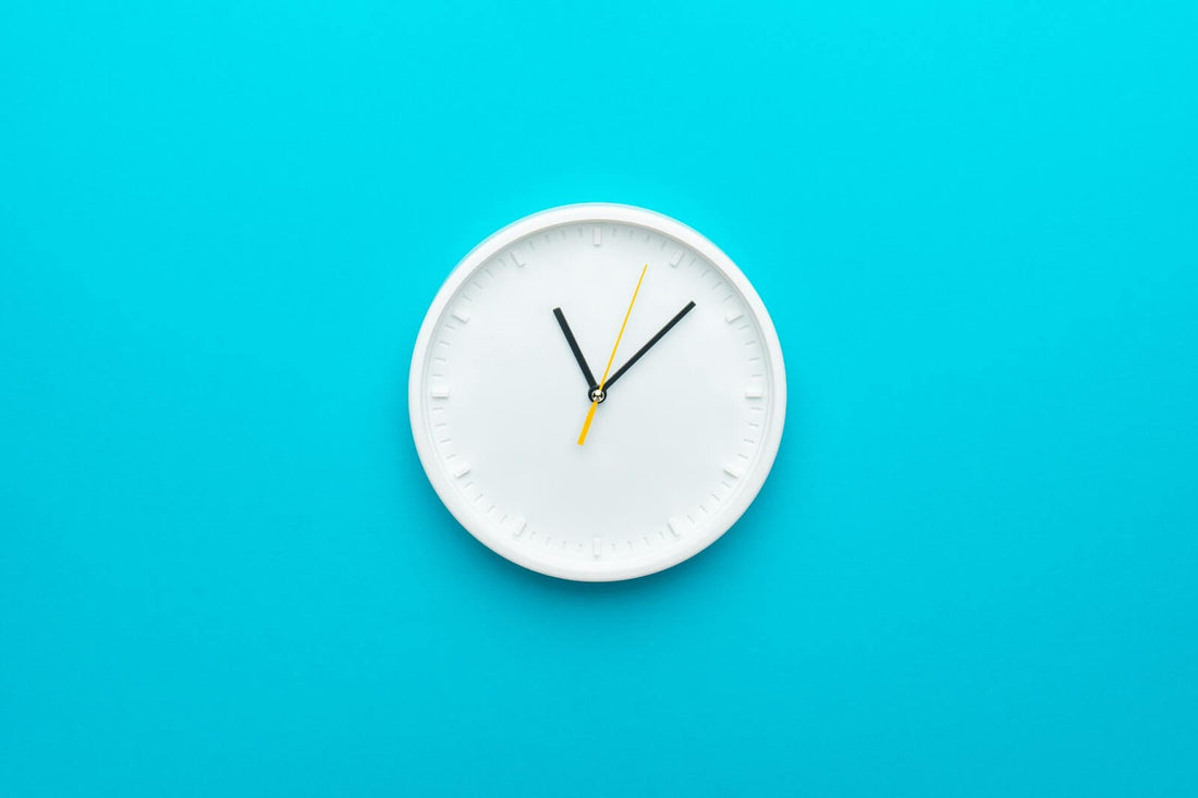 White wall clock centered on bright turquoise background with black hour and minute hands and a yellow second hand