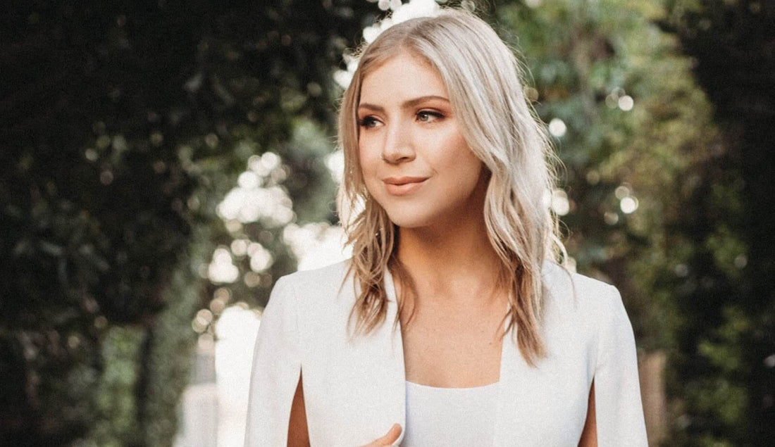 Blonde woman smiling and looking to the right in a sunlit garden with blurred trees