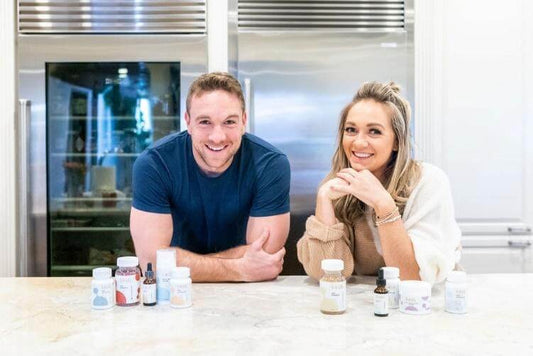 Two people smiling and leaning on a bright kitchen counter with several CBD product bottles displayed in front of them