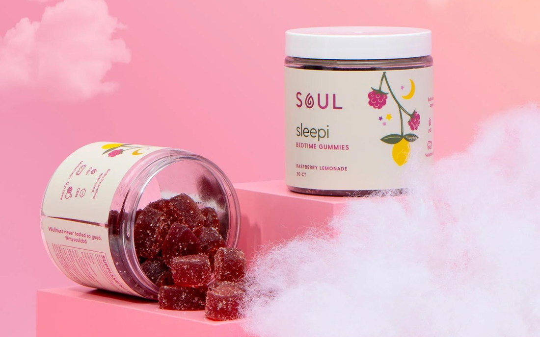 Front view of Soul Sleepi bedtime gummies jar and an open jar spilling raspberry lemonade sugar coated gummies on a pink background