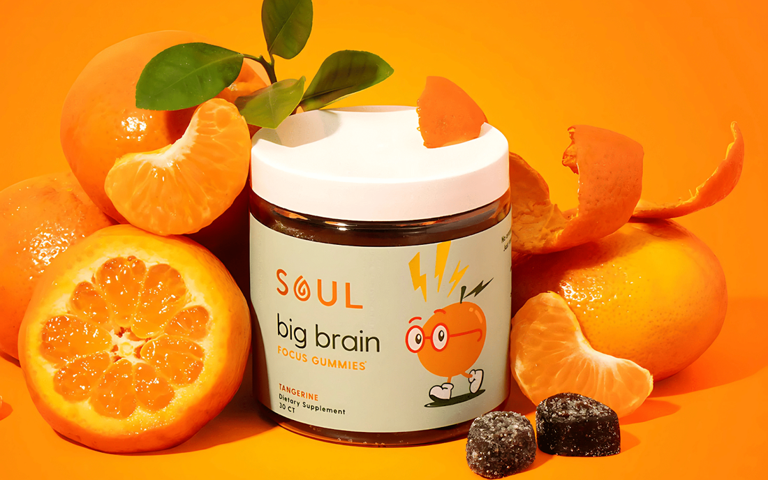 Front view of Soul Big Brain Focus Gummies jar with Tangerine label, tangerines and two sugared gummies on orange background
