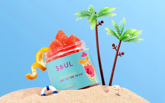 Angled jar of Soul Sex on the Beach CBD gummies showcasing red sugar-coated gummies and tropical label on a sandy beach background