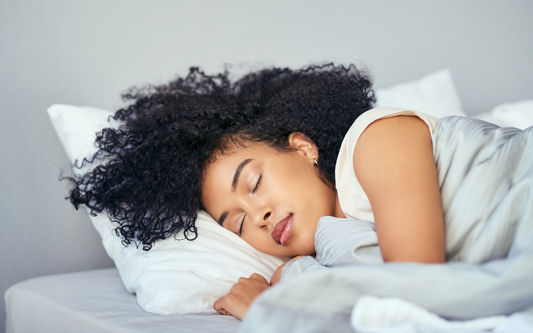 Young woman sleeping on her side in bed with a white pillow and light gray duvet