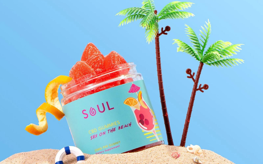 Angled jar of Soul CBD gummies labeled Sex on the Beach showing red sugar coated gummies on sand with toy palm trees
