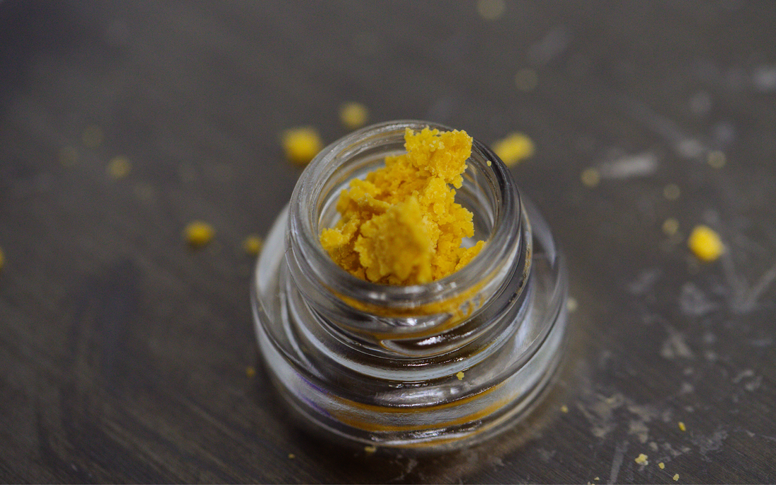Top-down view of yellow THC concentrate crumble in a small glass jar on a dark tabletop
