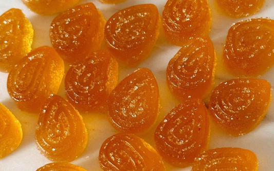 Close-up of orange teardrop mushroom gummies with visible sugar crystals on a white background