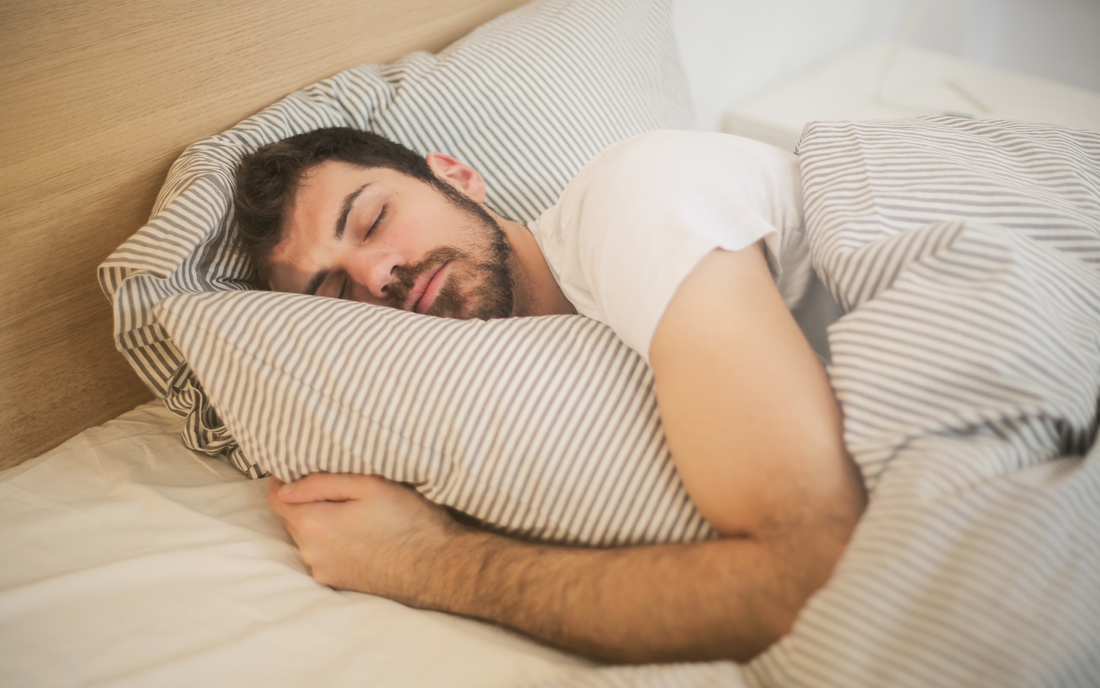 Man sleeping on his side hugging a striped pillow with matching striped duvet in a bedroom
