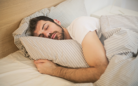 Man sleeping on his side hugging a striped pillow with matching striped duvet in a bedroom