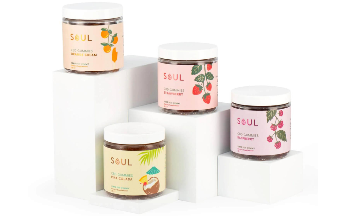 Front view of four Soul CBD gummies jars showing Orange Cream, Strawberry, Piña Colada, and Raspberry labels on white display blocks