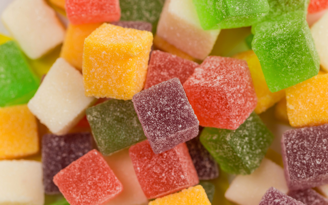 Close-up of sugar-coated gummy cubes showcasing assorted colors and granular sugary texture on a blurred background