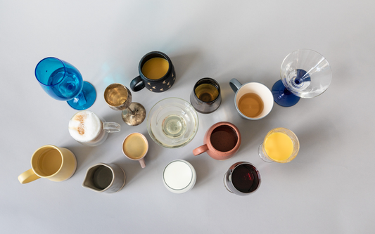 Overhead assortment of mugs, wine glasses, and tumblers each filled with different nonalcoholic beverages on a light gray background