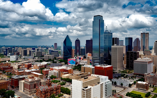 Aerial view of downtown Dallas with glass skyscrapers, red-brick historic courthouse in the foreground, and dramatic cloudy sky