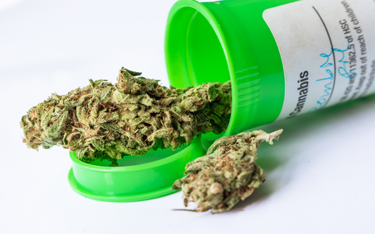 Close-up of cannabis buds spilling from a green prescription-style container on a white background
