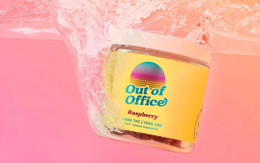 Tilted front view of Out of Office Raspberry gummy jar showing label with 1.5MG THC and 15MG CBD, colorful sunset logo, pink background with water splash