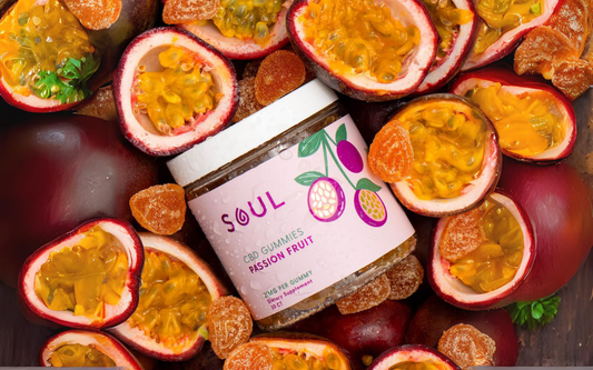 Angled top-down view of a jar of Soul Passion Fruit CBD gummies with label, surrounded by halved passion fruit and gummies