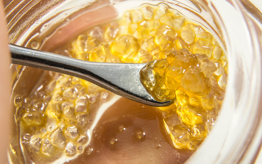 Macro close-up of THCA crystal concentrate on a metal dab tool showcasing glossy amber bead-like texture in a glass jar