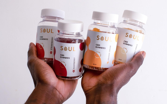 Close-up of four SOUL CBD Gummies bottles in hands showing strawberry, raspberry, orange cream, and coconut vanilla labels
