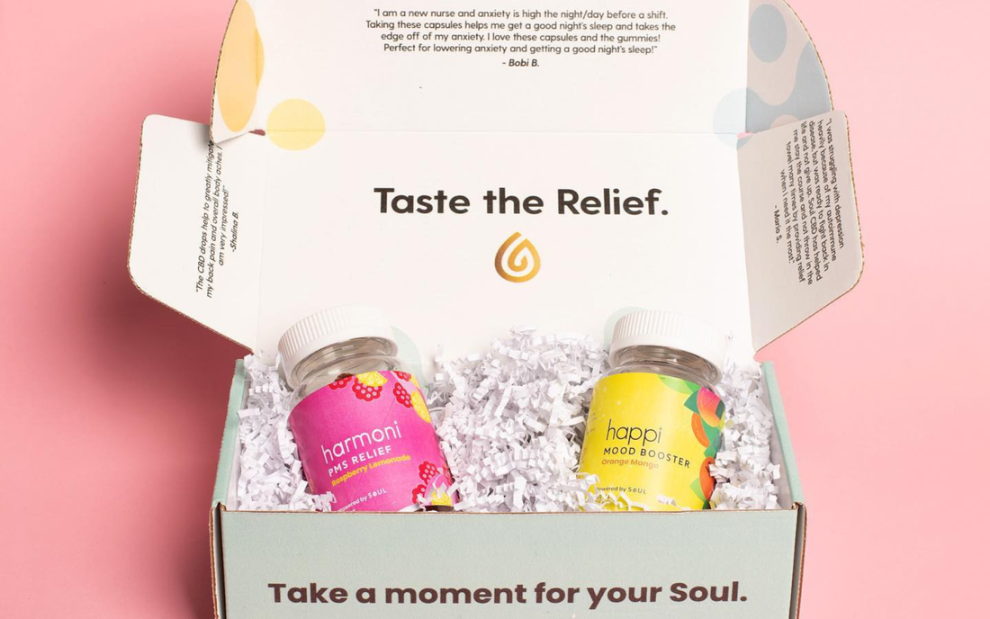 Two colorful supplement jars nestled in white crinkle paper inside an open mint gift box on a pink background