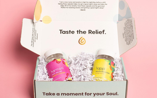 Two colorful supplement jars nestled in white crinkle paper inside an open mint gift box on a pink background