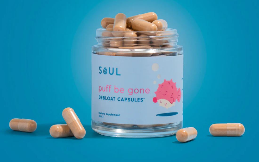 Front view of Puff Be Gone debloat capsules jar showing label puff be gone and loose beige capsules on blue background