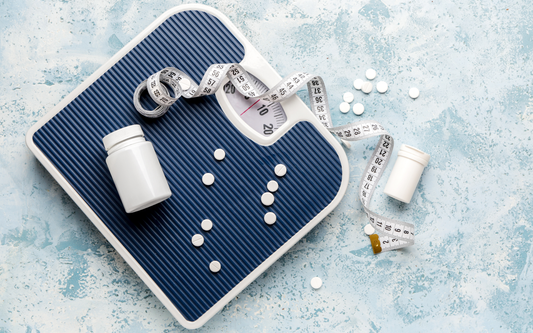 Bathroom scale surrounded by pill bottles, scattered white tablets, and a measuring tape on a textured blue background