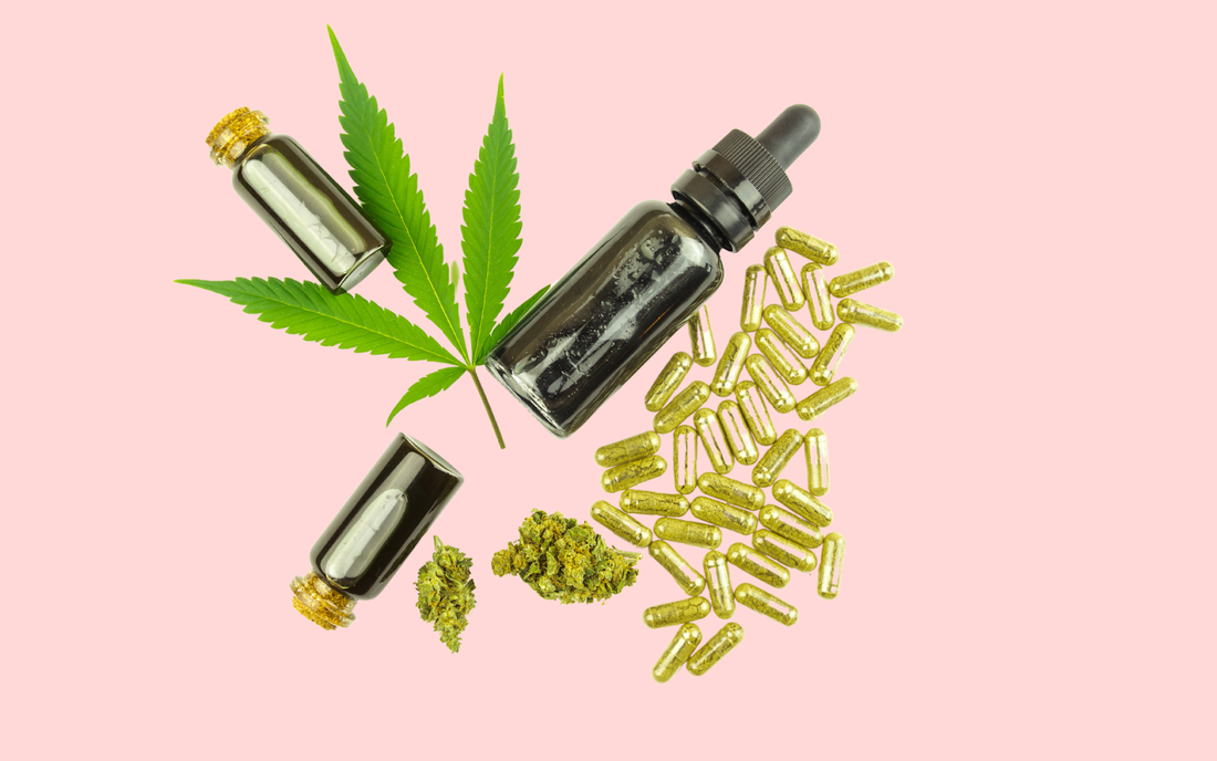 Cannabis leaf with dropper oil bottle, two small glass vials, dried buds and golden capsules arranged on a pink background