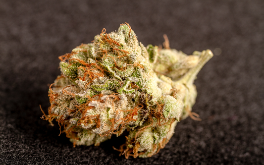Close-up of THCP cannabis bud showing frosty trichomes and orange pistils on a dark textured background