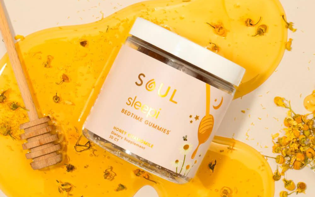 Tilted jar of Soul Sleepi bedtime gummies showing white lid and label with honey spill and chamomile flowers background