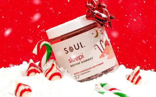 Angled jar of Soul Sleepi bedtime gummies showcasing white chocolate peppermint label and red gift bow against a snowy red background