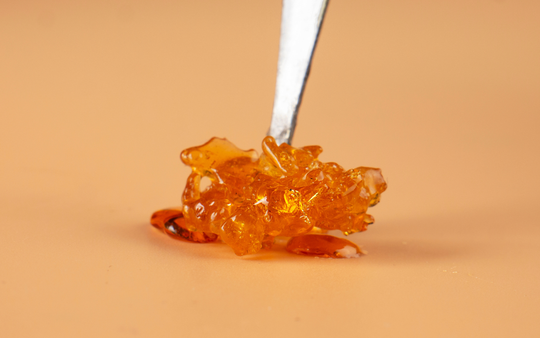 Close-up of THC distillate on a metal dab tool showing amber, glass-like, glossy texture on a peach background