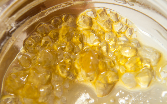 Close-up of amber cannabis terpene crystals in a glass jar showing glossy, honey-colored resin texture