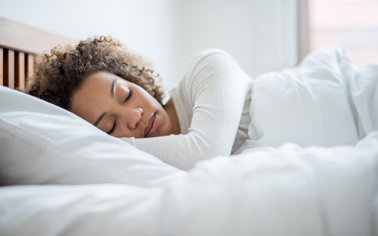 Woman sleeping on her side in a bright bedroom, tucked under a white duvet
