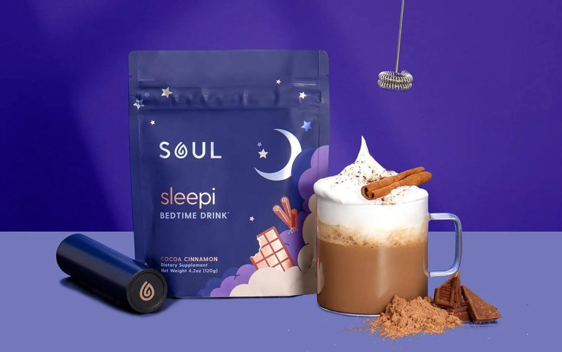 Front view of Sleepi pouch and cocoa cinnamon mug with frothed top and cinnamon stick on purple background