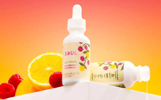 Front view of Soul Raspberry Lemonade CBD drops bottle showing label and “1500mg per bottle” with raspberries, an orange slice, and orange-to-pink gradient background
