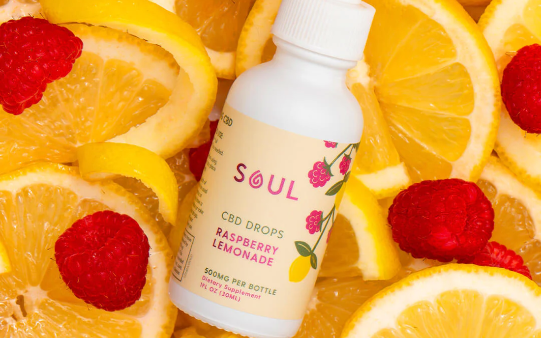 Angled bottle of Soul CBD Drops Raspberry Lemonade showcasing flavor label with sliced lemons and raspberries background