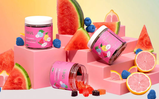 Close-up of three Soul CBD gummy jars showing spilled gummies and pink fruit packaging on a stepped pink display
