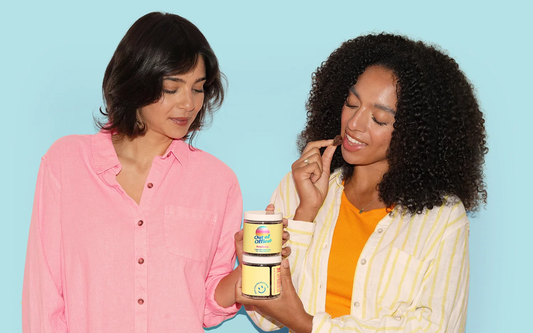 Two women sharing and sampling Out of Office raspberry gummies against a pale blue background