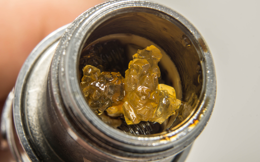 Close-up top-down view of THCA crystalline cannabis concentrate showing amber, glassy crystalline nuggets inside a metal dab container