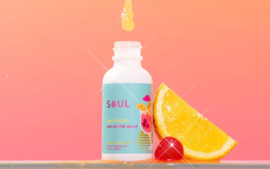 Front view of Soul CBD Drops ‘Sex on the Beach’ bottle showing label, orange slice and cherry on pink gradient background