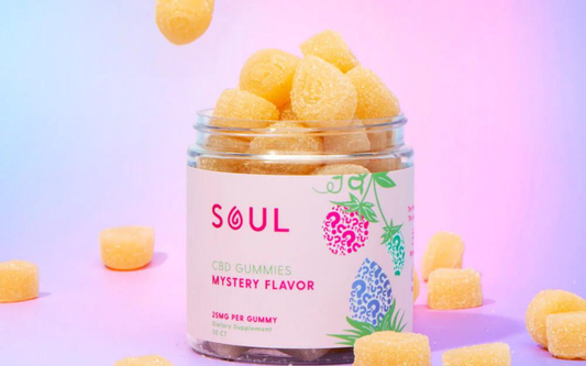 Front view of Soul CBD Gummies jar showcasing sugar coated yellow gummies and label reading SOUL Mystery Flavor with pastel pink and blue gradient background