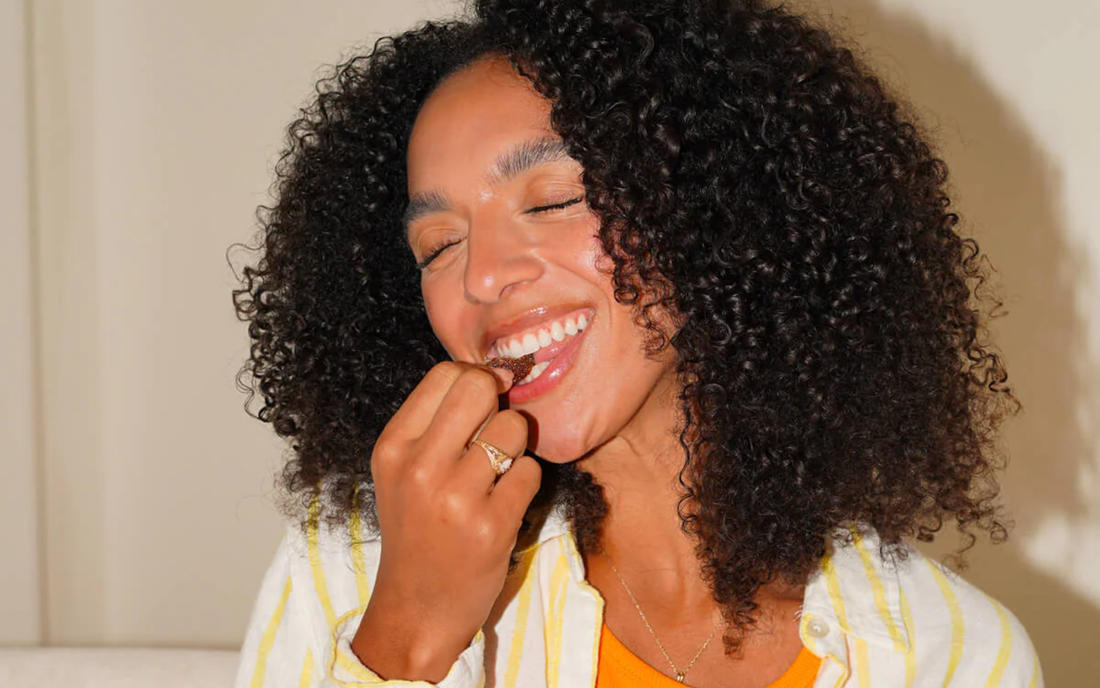 Woman smiling with eyes closed eating a CBD gummy in a bright indoor setting