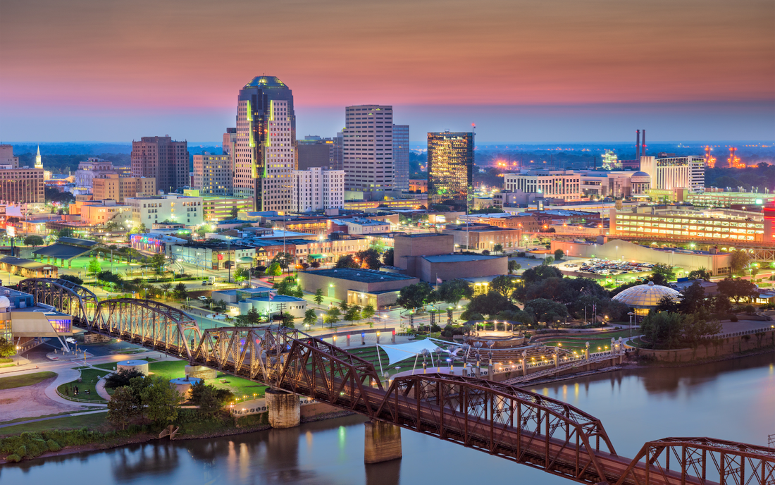 Baton Rouge skyline at dusk with illuminated downtown buildings and an iron truss bridge over the Mississippi River