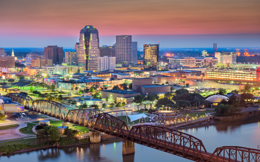 Baton Rouge skyline at dusk with illuminated downtown buildings and an iron truss bridge over the Mississippi River