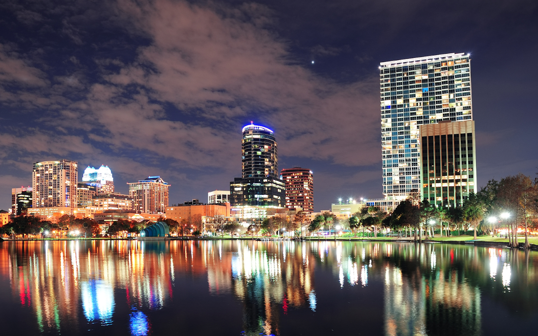 Nighttime city skyline with illuminated high-rise buildings reflecting in a calm lake